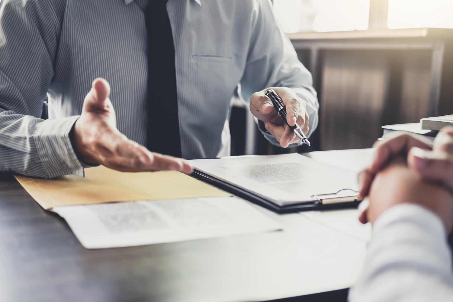 man at desk wearing black tie and gray shirt with pen and customer signing business insurance paperwork